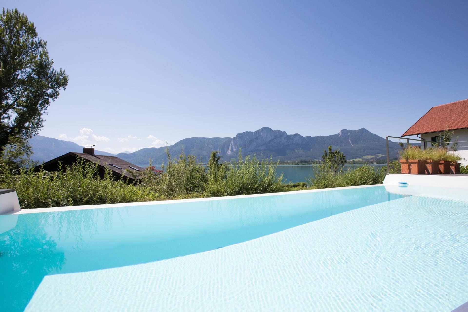 Erfrischender Poolbereich mit unverbautem Blick auf den glitzernden See und die majestätischen Berge.