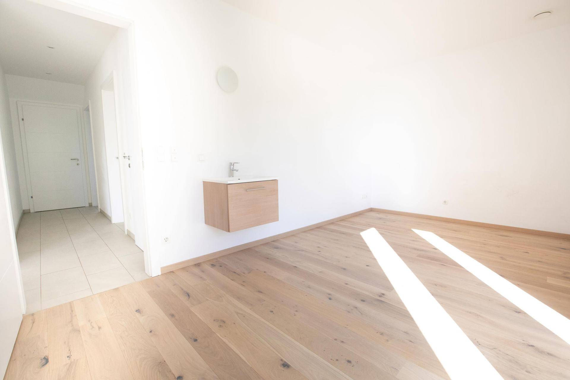 Helles Zimmer mit Holzboden und einem schwebenden Waschbecken, bereit zur individuellen Gestaltung.