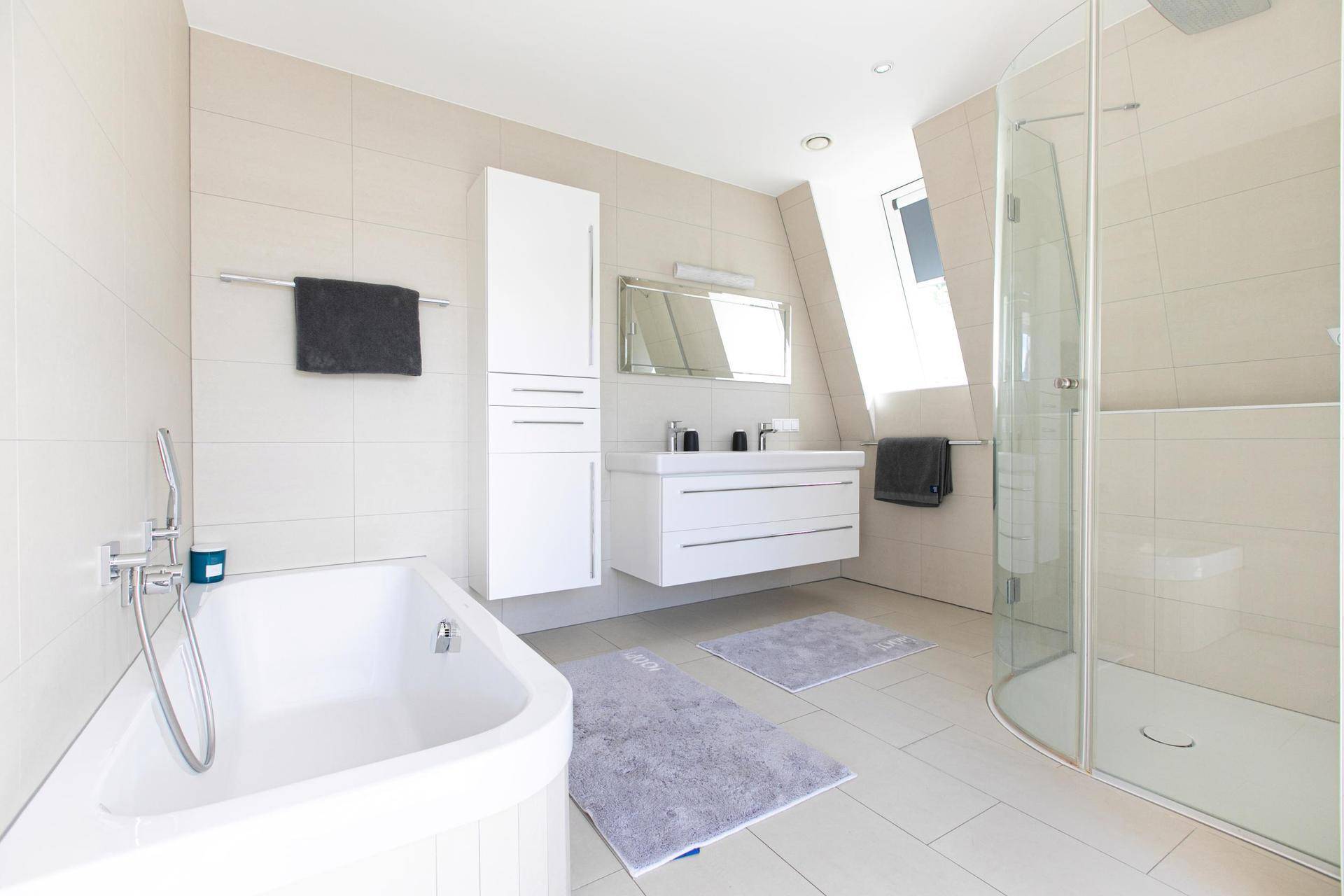 Modernes Badezimmer mit Badewanne, Duschkabine, Doppelwaschbecken und hellen Fliesen.