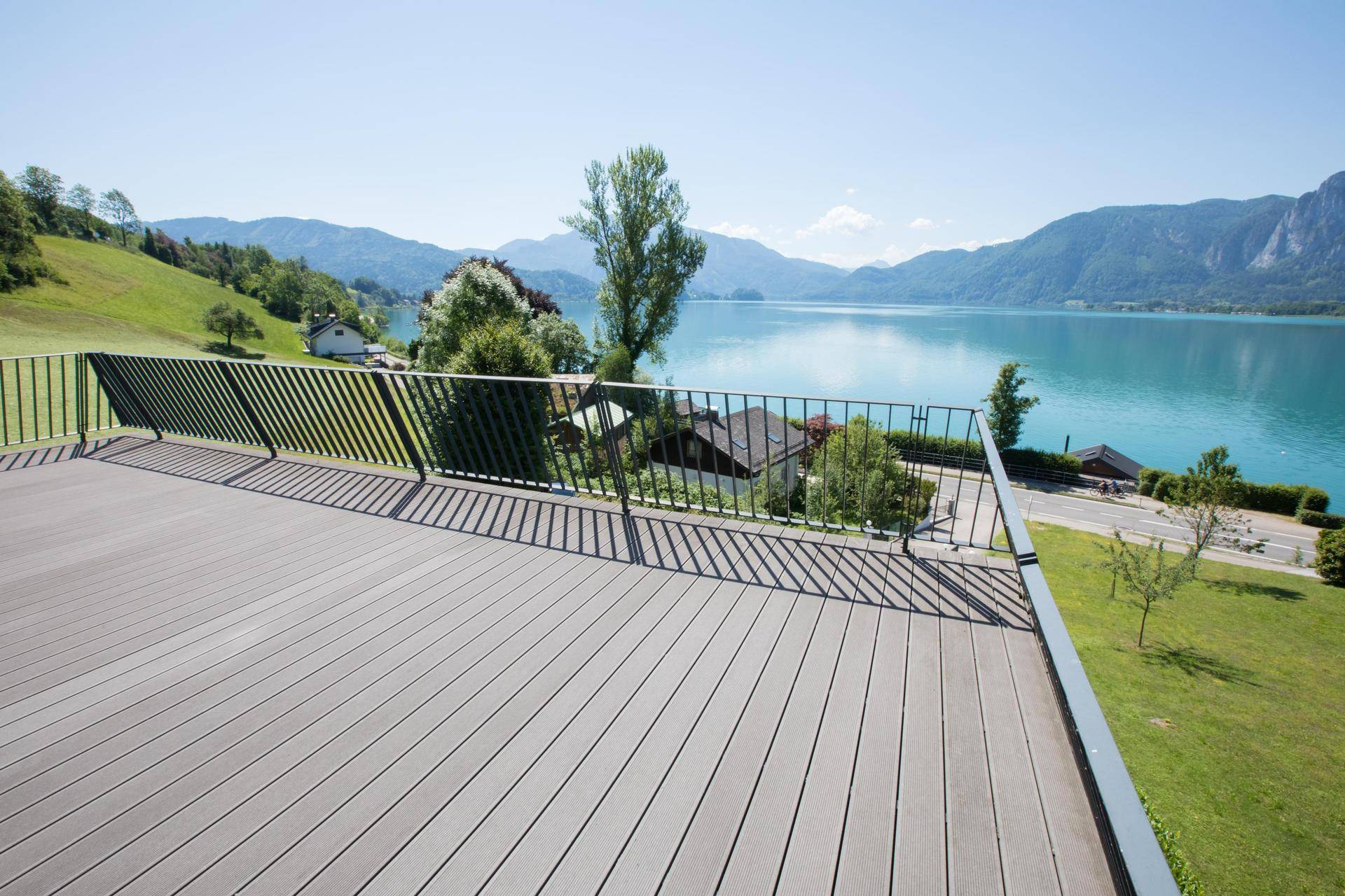 Große Holzterrasse mit dunklem Geländer, die einen weiten Blick auf den See und die Umgebung bietet.