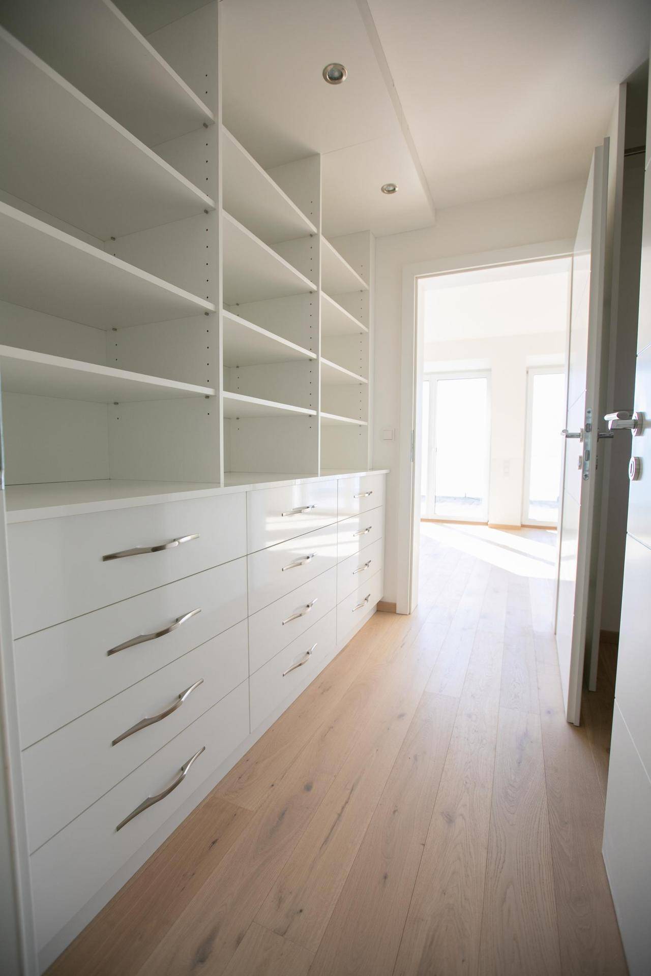 Geräumiger begehbarer Kleiderschrank mit weißen Einbauschränken und viel Stauraum.