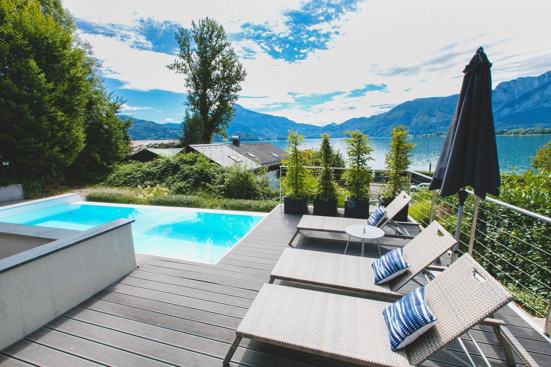 Geräumige Terrasse mit Pool und bequemen Liegestühlen, die einen atemberaubenden Blick auf den See und die Berge bietet.