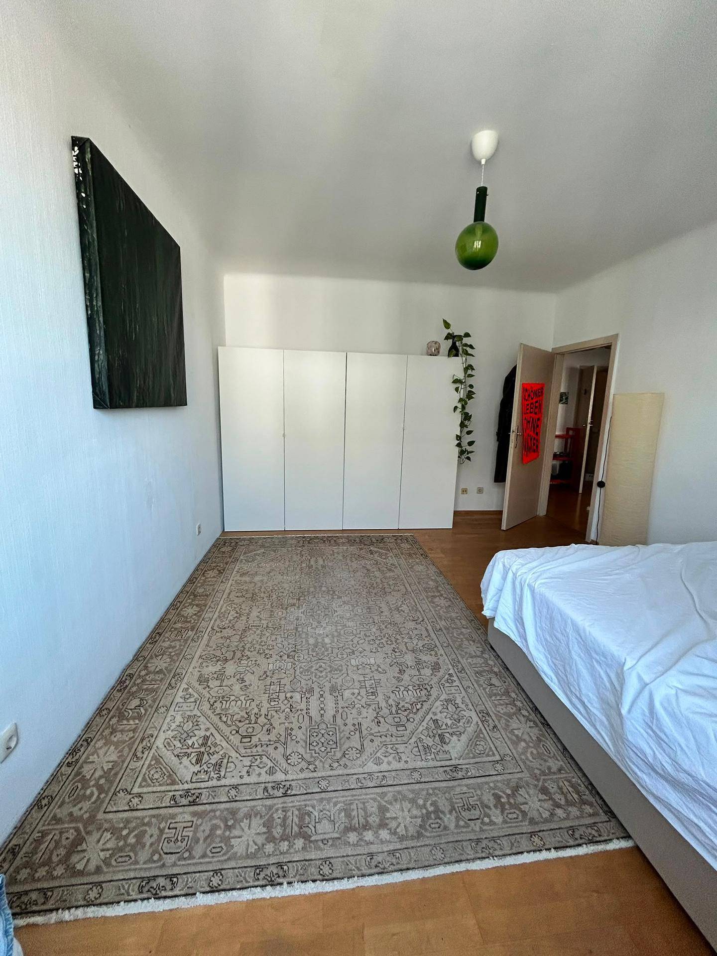 Geräumiges Schlafzimmer mit weißem Kleiderschrank, Holzboden und einem großen Teppich.