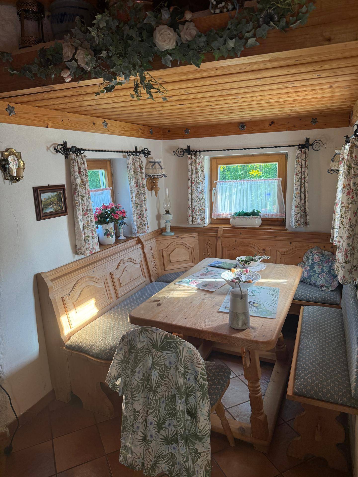 Gemütlicher Essbereich im Landhausstil mit Holzbänken, Holztisch und floralen Vorhängen.