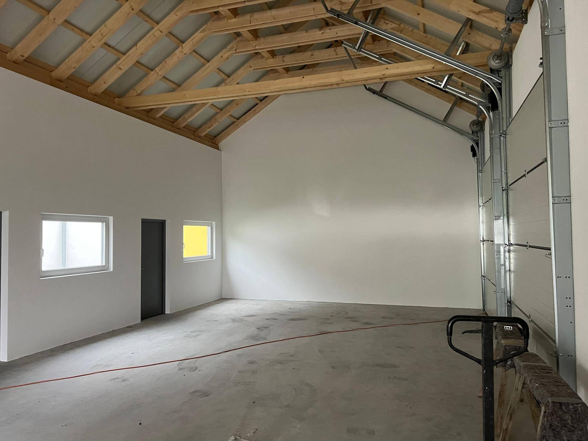 Heller Innenraum mit weißen Wänden, Fenstern und der beeindruckenden Holz-Dachkonstruktion.