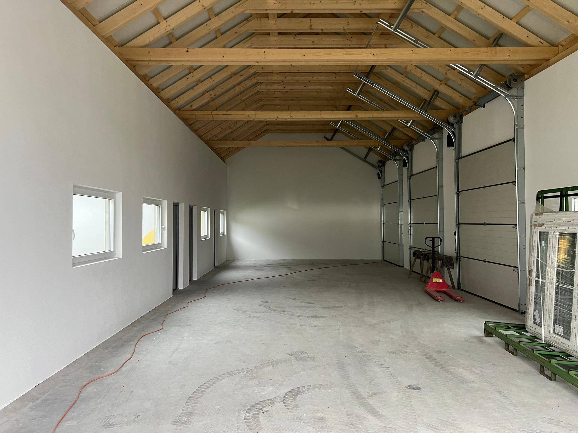 Geräumiger Innenraum mit Betonboden, weißen Wänden und sichtbarer Holz-Dachkonstruktion.