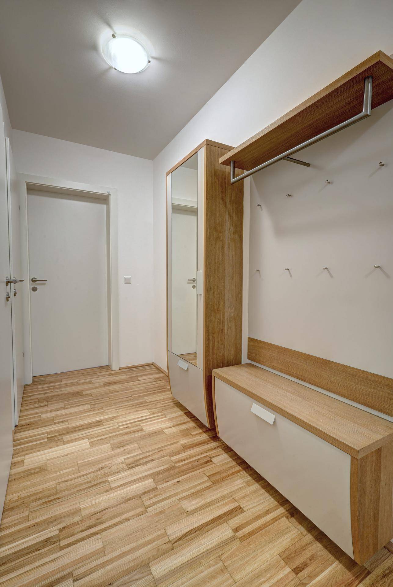 Heller Flur mit Holzfußboden und praktischer Garderobe mit Spiegel und Sitzbank.
