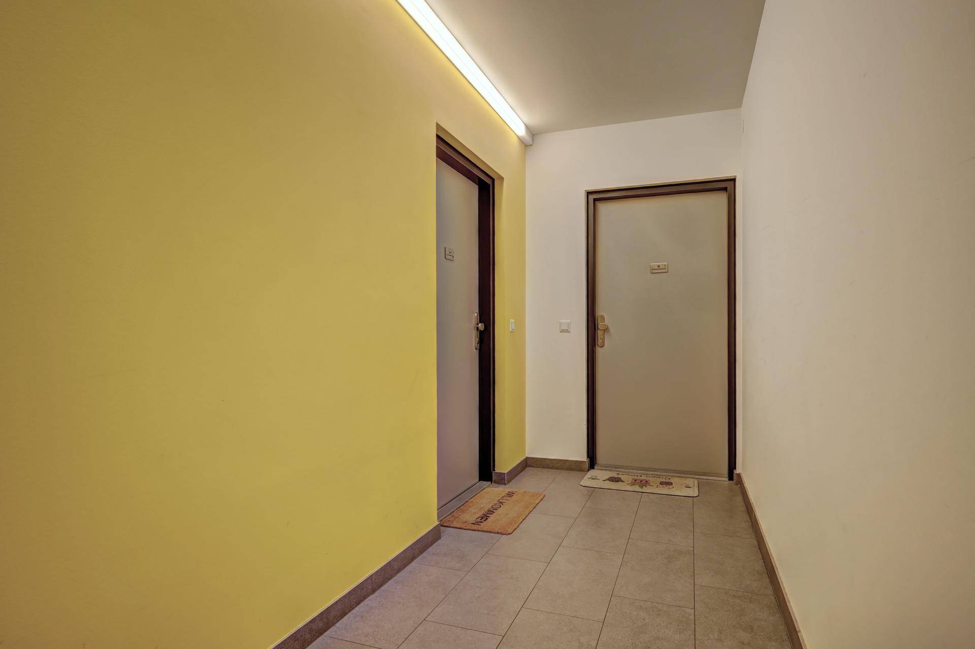 Heller Hausflur mit Fliesenboden und einer gelben Akzentwand, führt zu den Wohneinheiten.