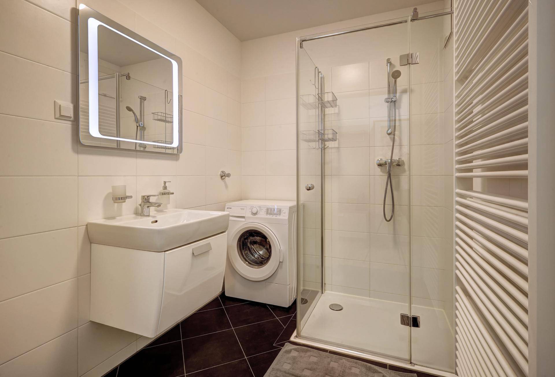 Modernes Badezimmer mit Duschkabine, Waschbecken, Waschmaschine und beheiztem Handtuchhalter.