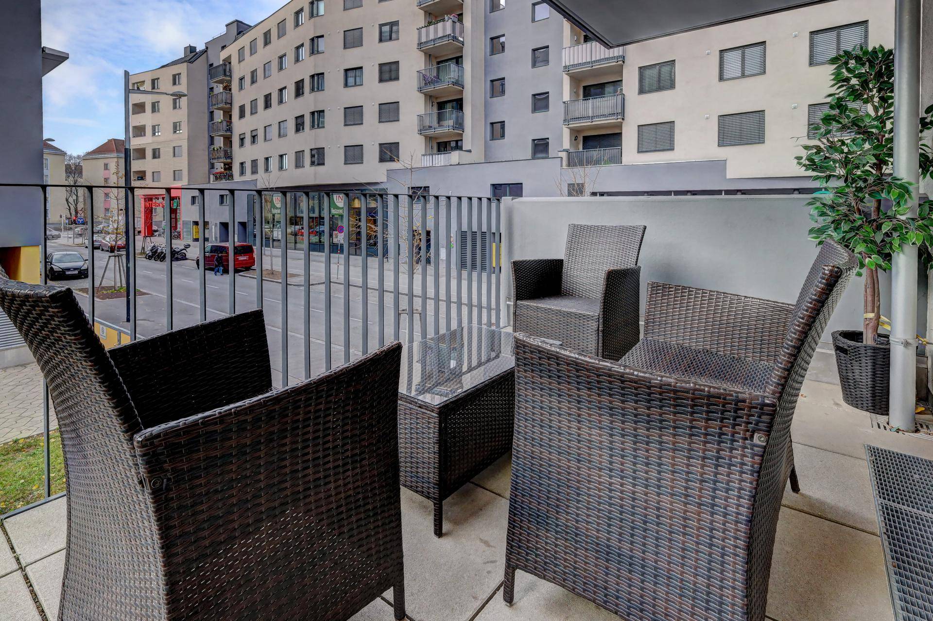 Möblierter Balkon mit Rattanmöbeln und Blick auf die umliegende Stadtlandschaft.