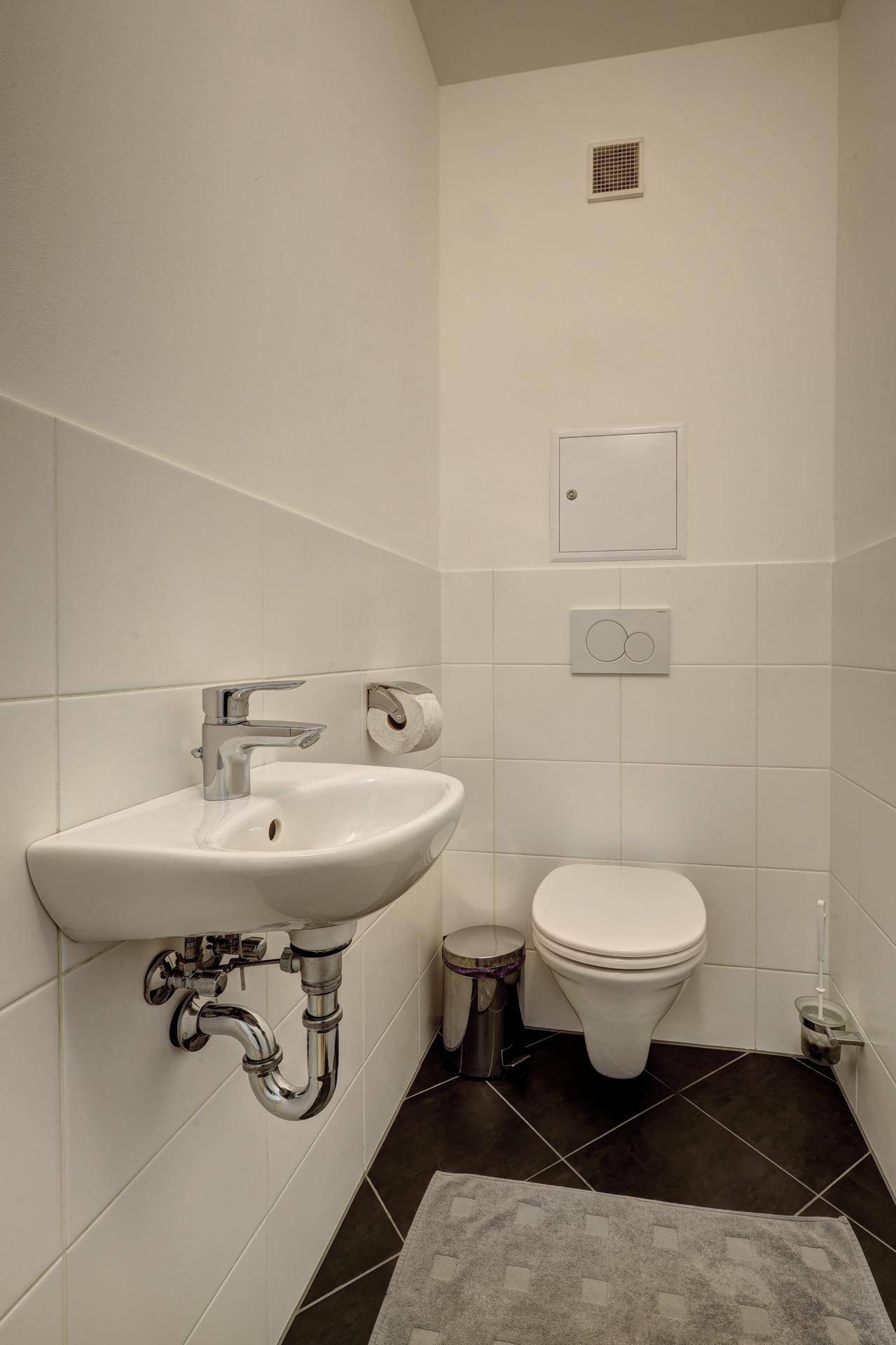 Kleines Gäste-WC mit wandhängender Toilette und kompaktem Eckwaschbecken, hell gefliest.