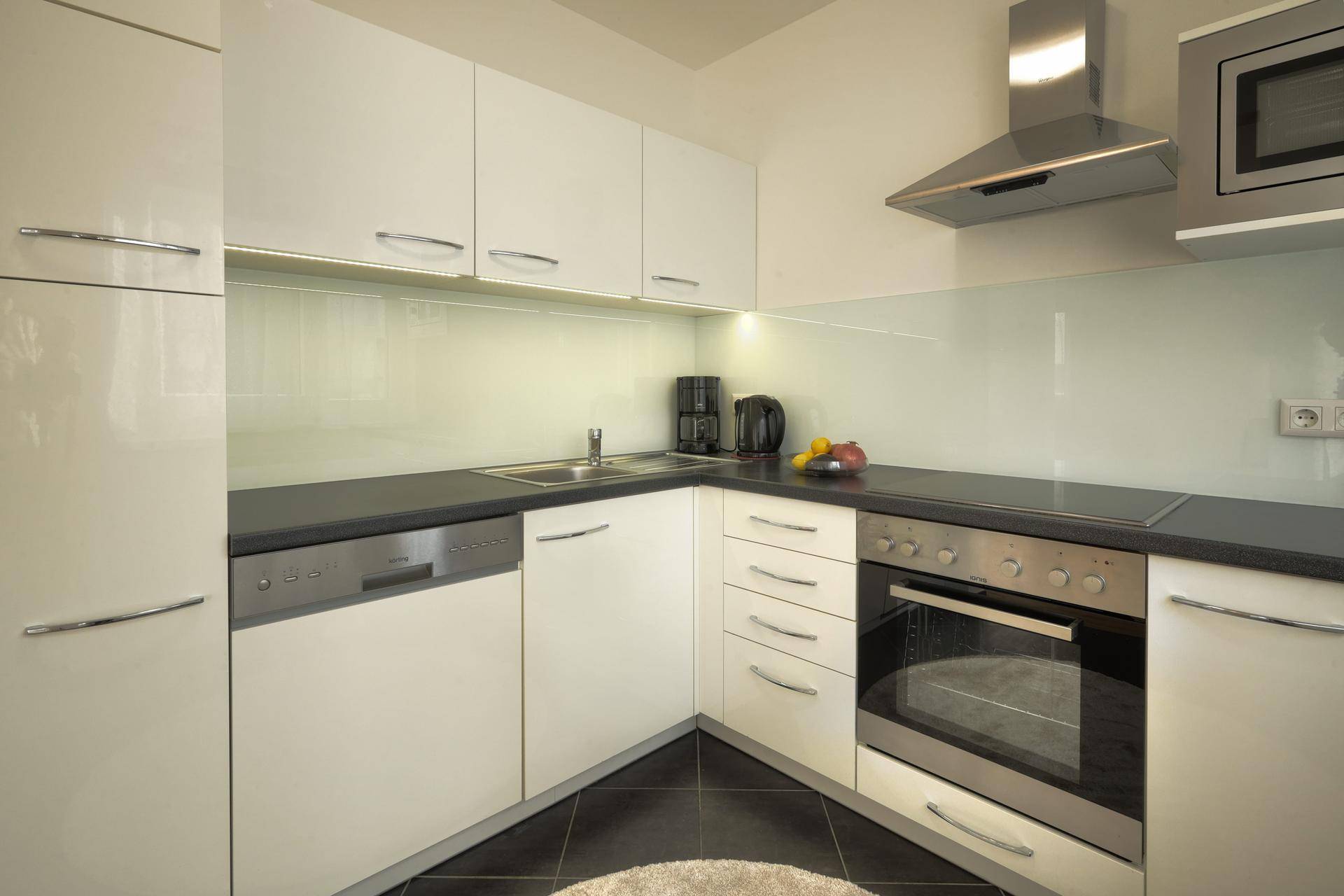 Moderne Einbauküche mit weißen Hochglanzfronten, dunkler Arbeitsplatte und integrierten Geräten.