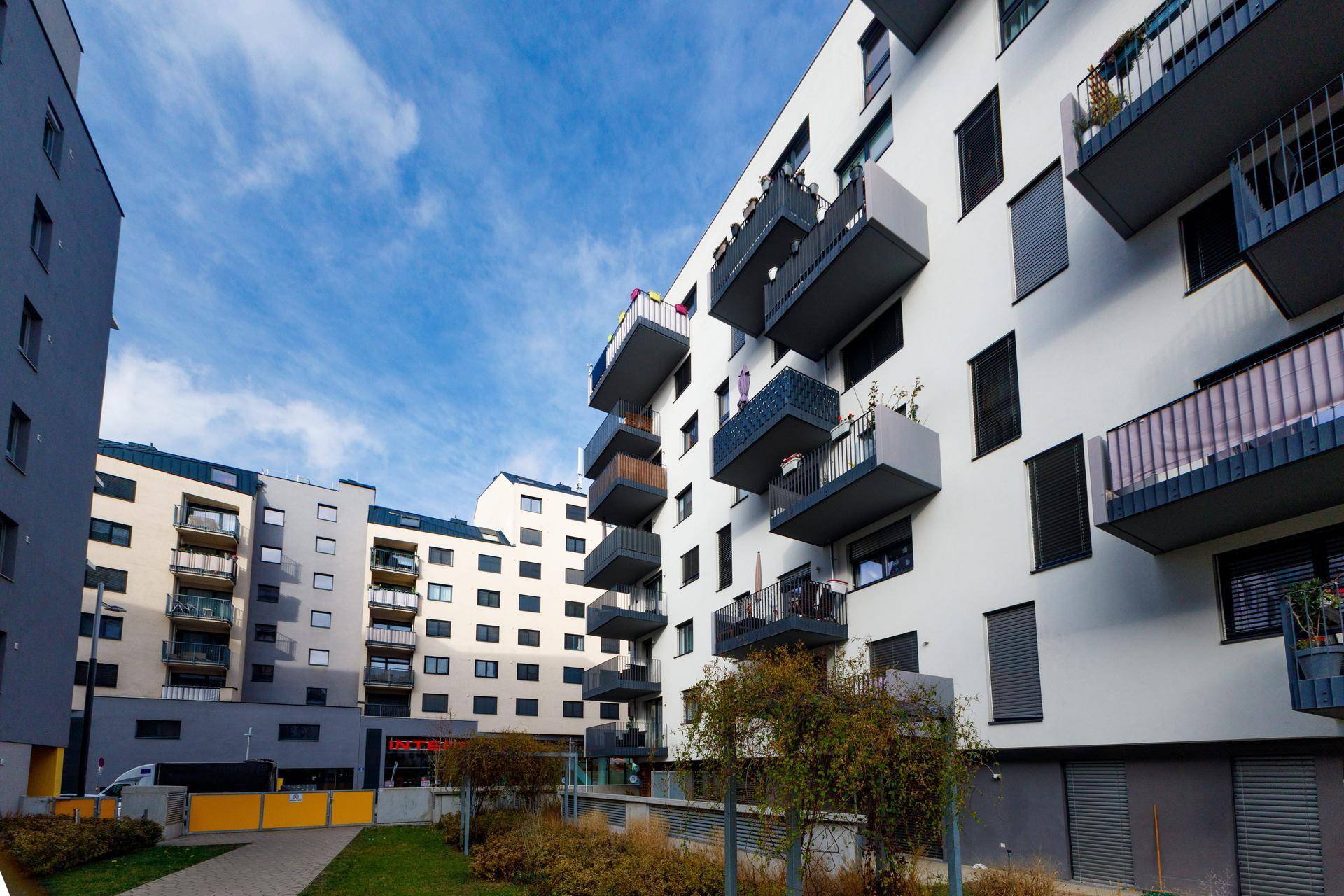Ansicht eines modernen Wohnkomplexes mit Balkonen und gepflegten Grünflächen im Außenbereich.