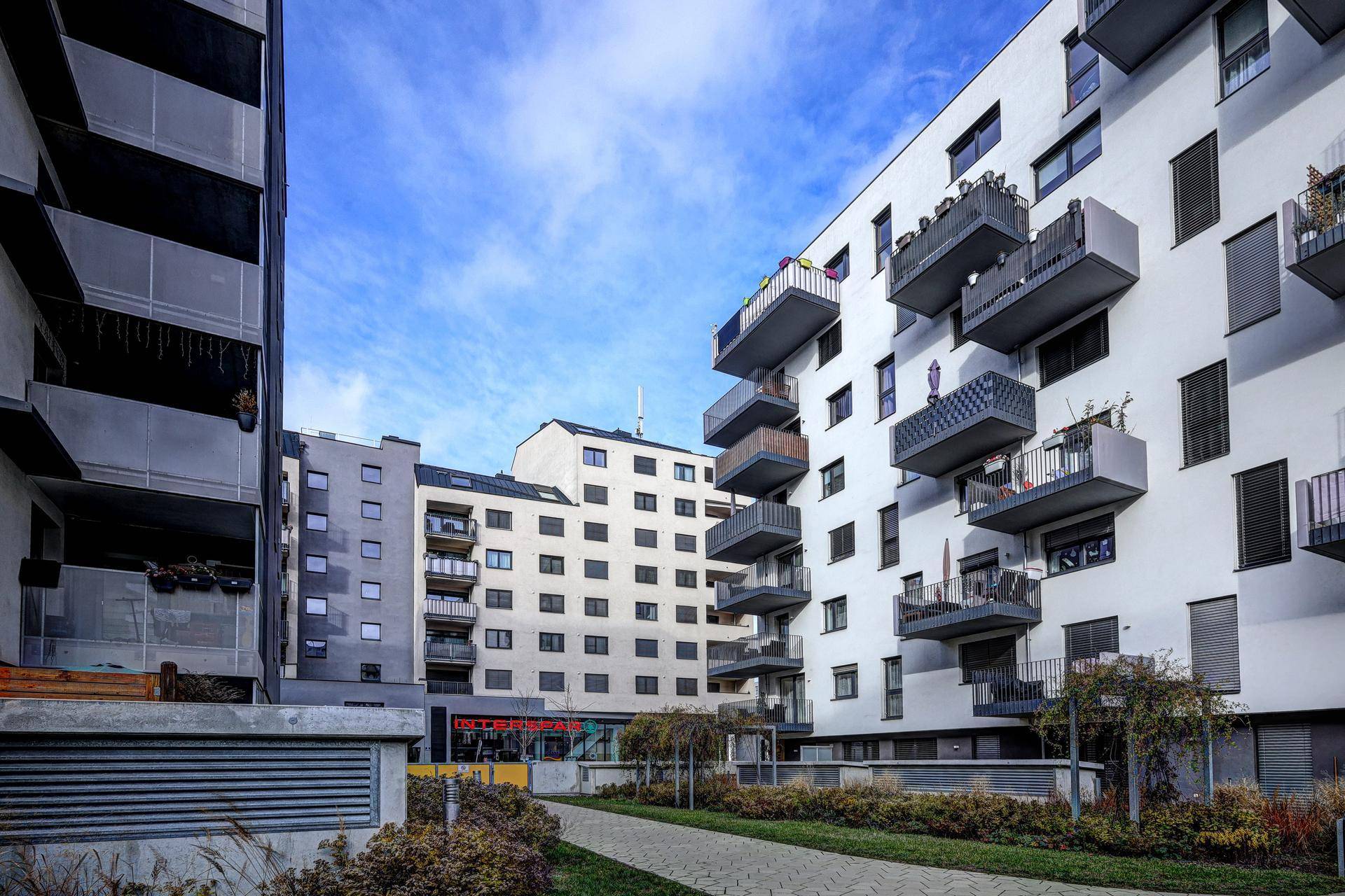 Moderne Wohngebäude mit zahlreichen Balkonen unter blauem Himmel und gepflegter Außenanlage.