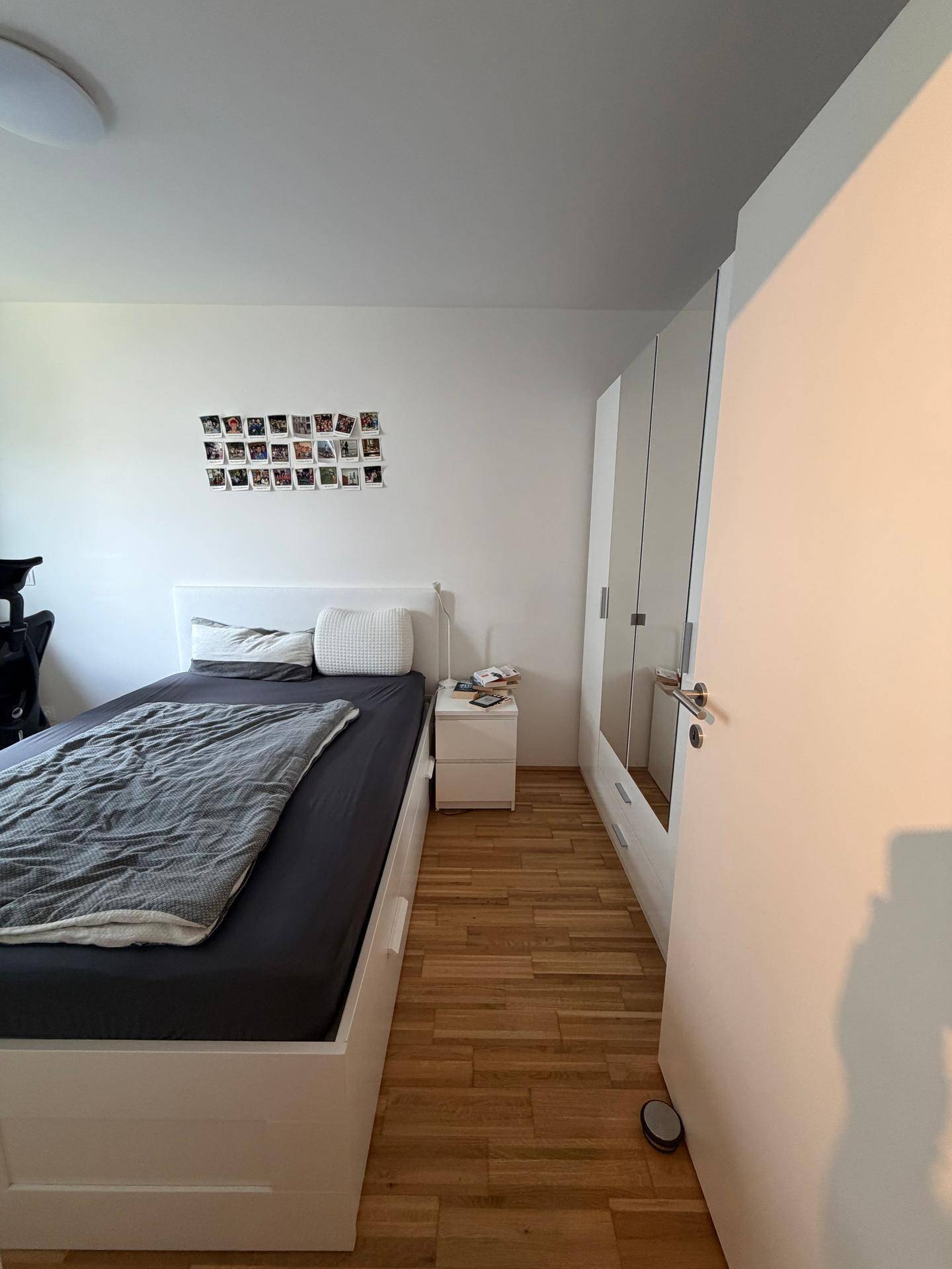 Schlafzimmer mit weißem Bett, Holzboden und praktischen Einbauschränken mit Spiegeltüren.