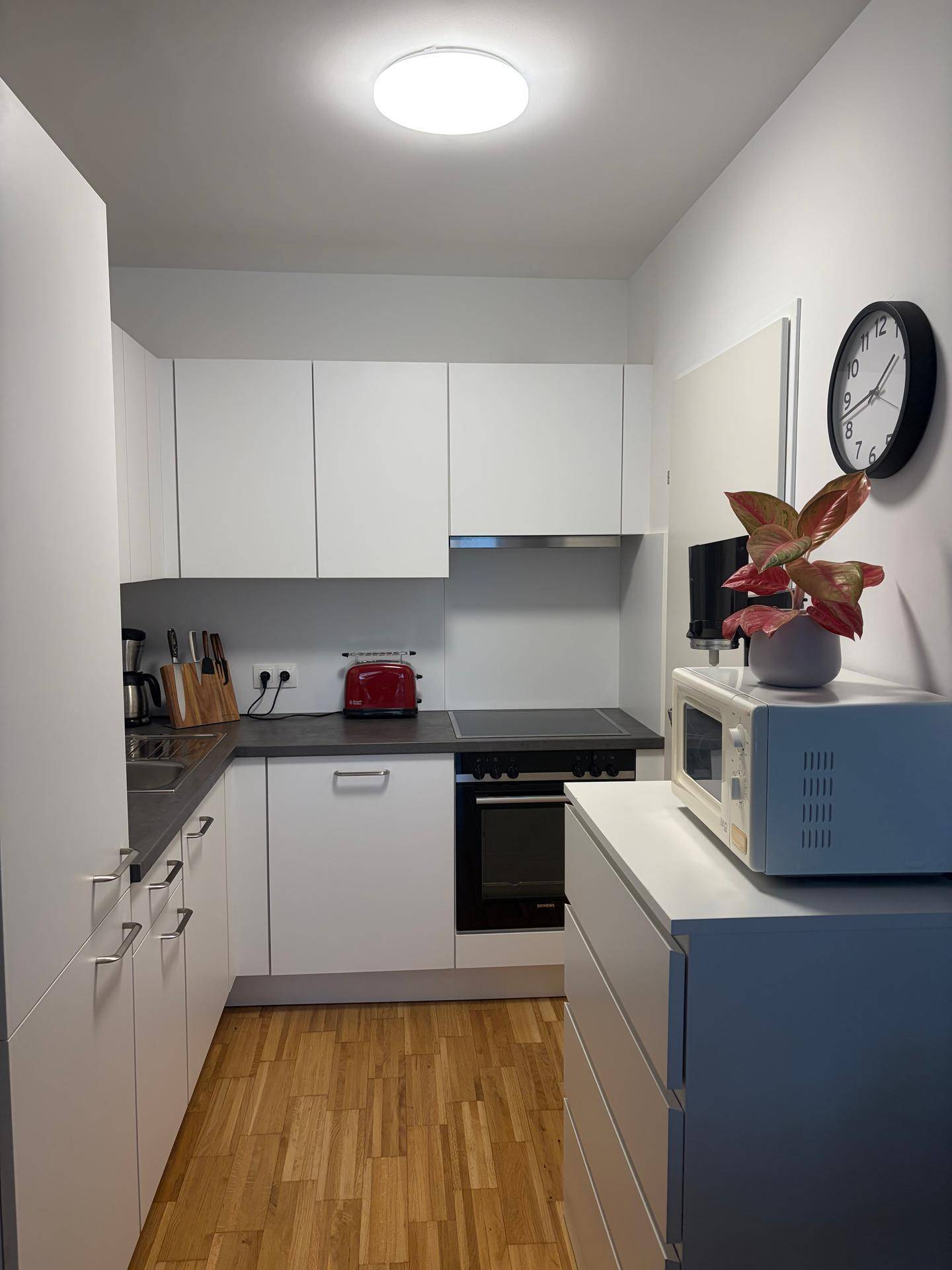 Moderne, kompakte Küche mit weißen Schränken, dunkler Arbeitsplatte und Holzboden.