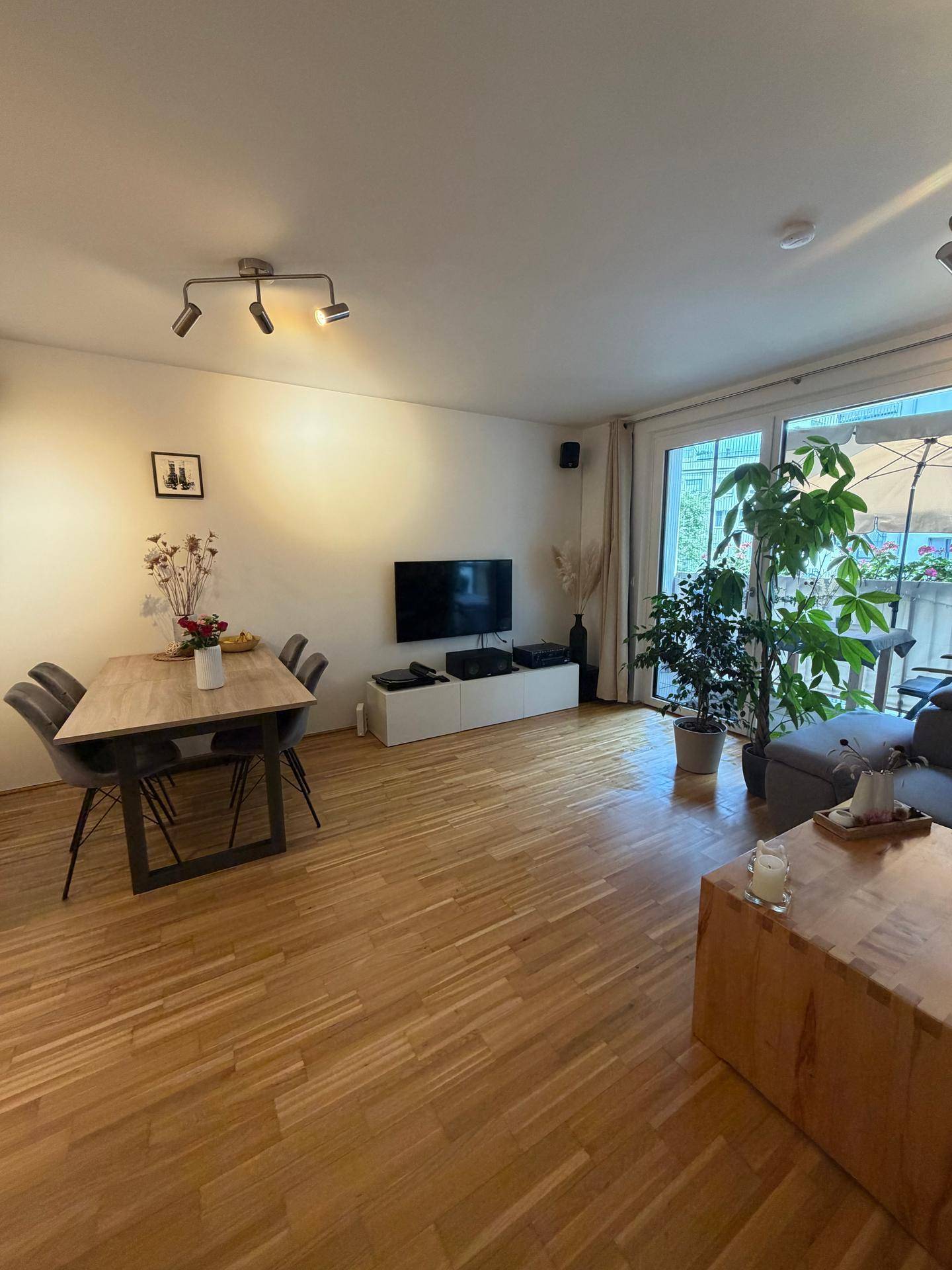 Offener Wohn-Essbereich mit Holzboden, Esstisch und Zugang zum Balkon.