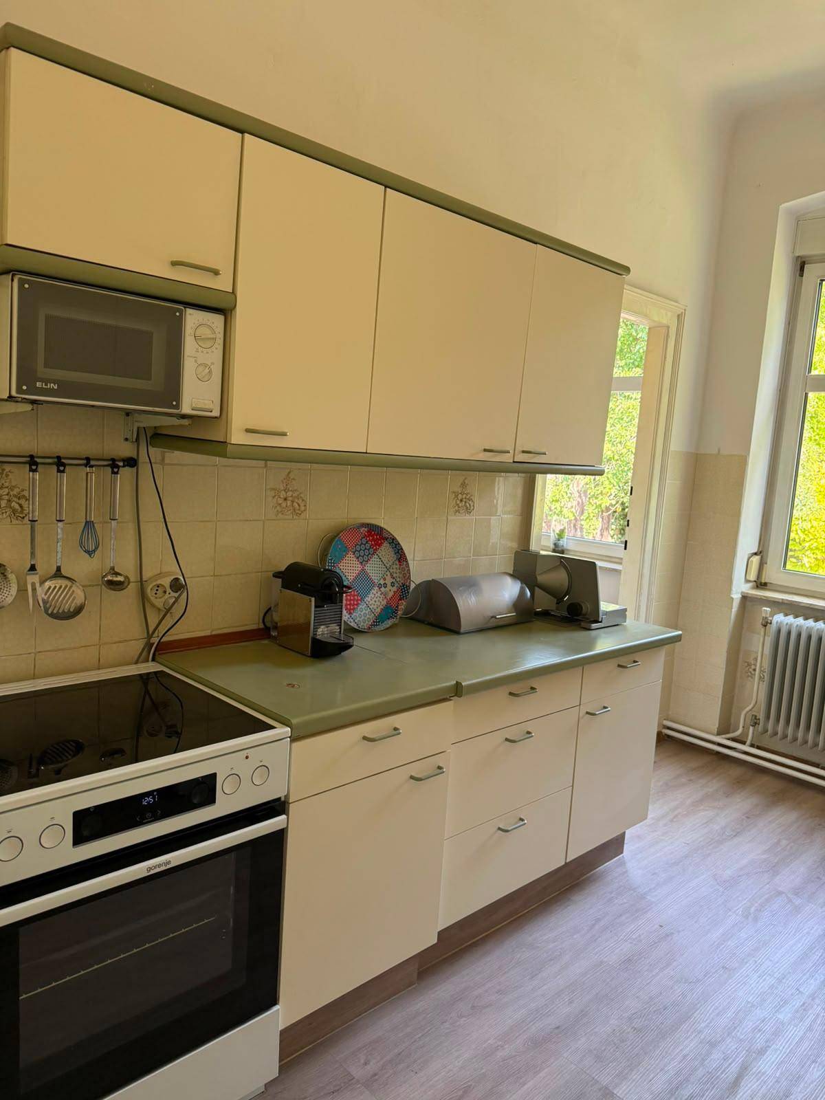 Küche mit hellgrünen Arbeitsplatten, cremefarbenen Schränken und einem Fenster mit Blick ins Grüne.