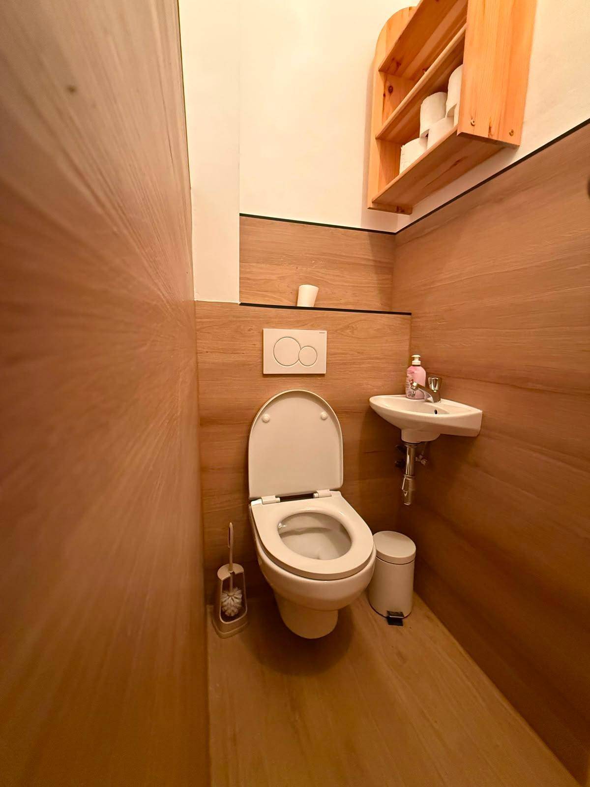 Gäste-WC mit Holzverkleidung, wandhängender Toilette und kleinem Waschbecken.