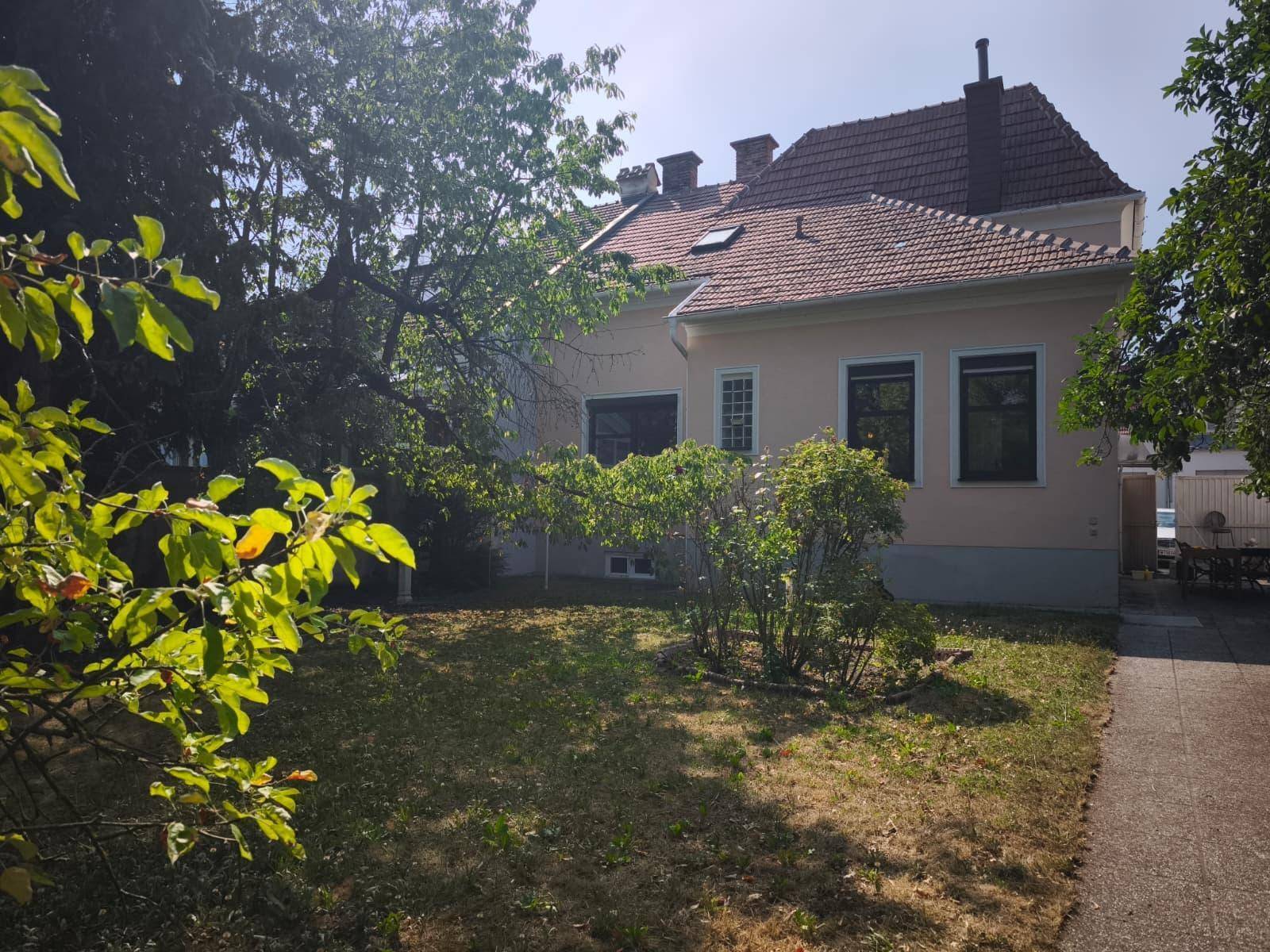 Rückansicht des Hauses mit hellrosa Fassade und einem gepflegten Garten mit Rasen und Büschen.