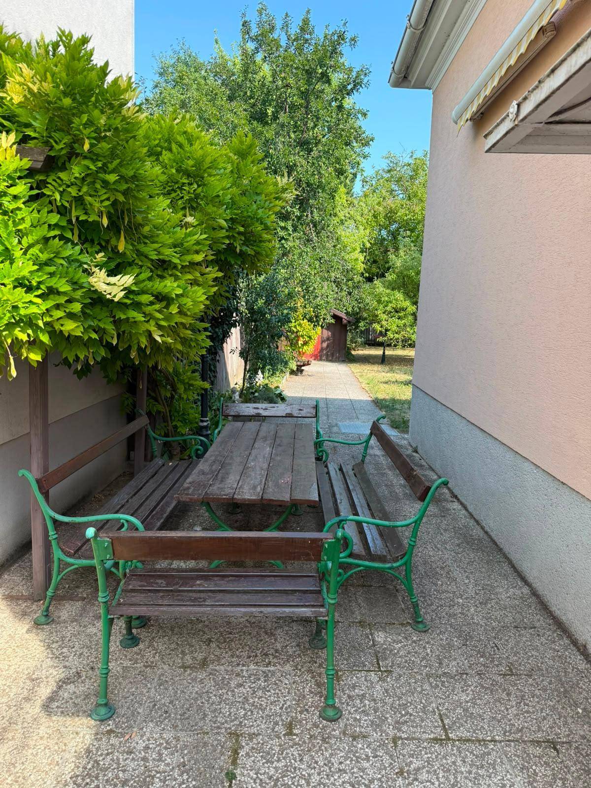 Gemütlicher Außenbereich mit gepflasterter Terrasse, Holztisch und grünen Gartenbänken zum Entspannen.