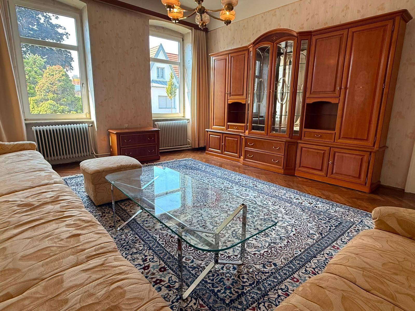 Gemütliches Wohnzimmer mit traditionellen Holzmöbeln, großem Teppich und einem Couchtisch aus Glas.
