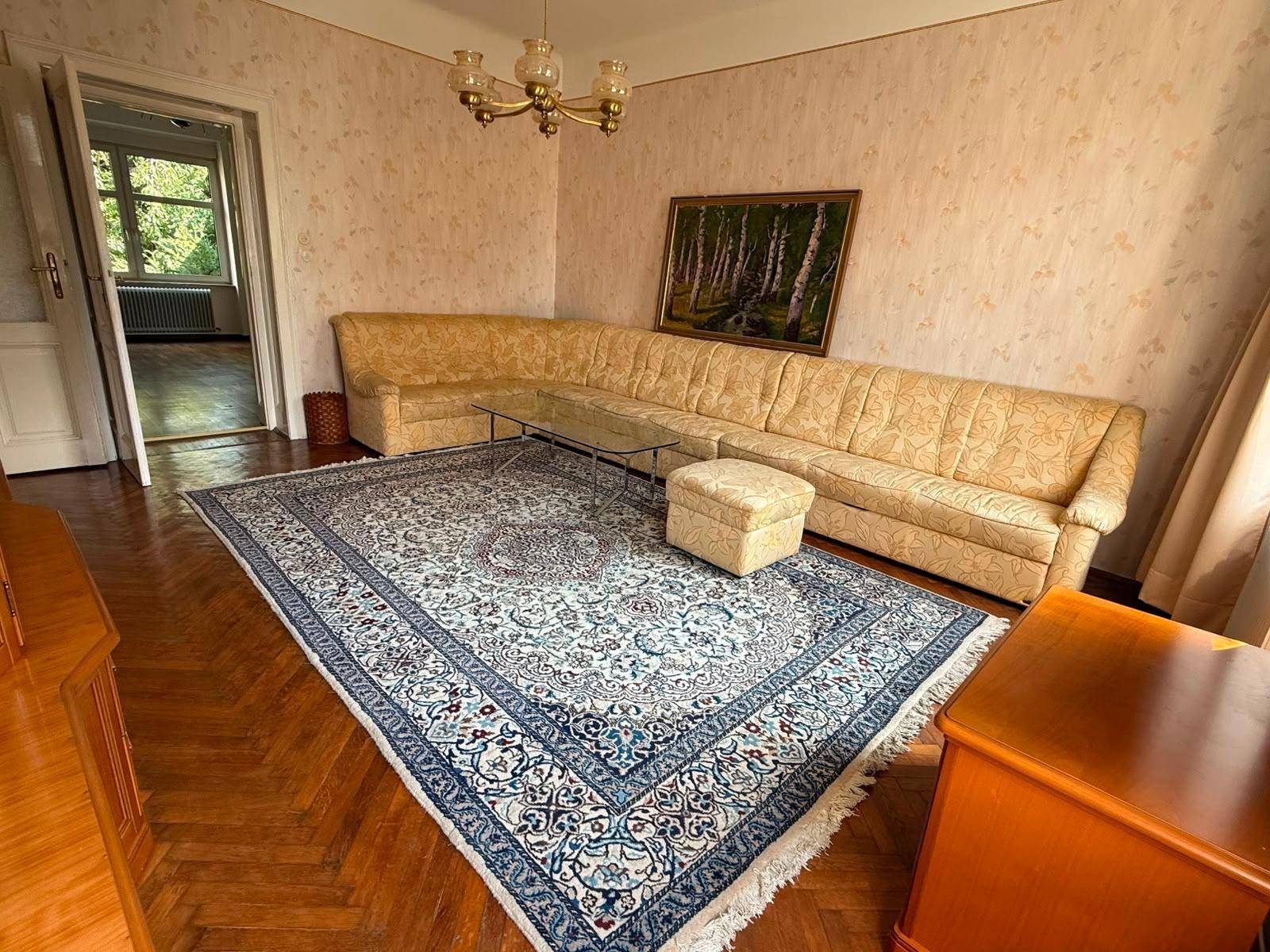 Wohnzimmer mit großem Ecksofa, gemustertem Teppich und einem Gemälde an der hellen Wand.