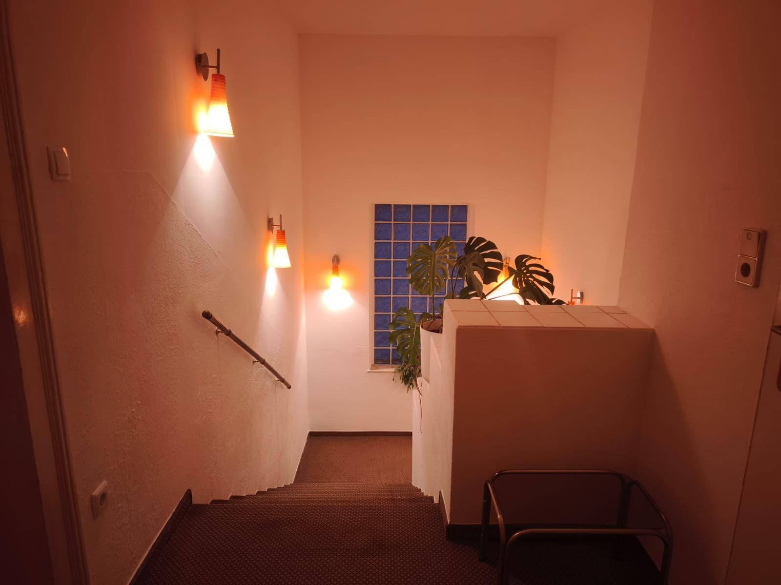 Treppenhaus bei Abendlicht mit beleuchteten orangefarbenen Wandleuchten und Glasbausteinfenster.