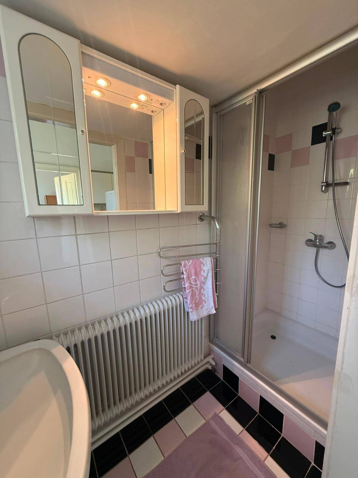 Badezimmer mit Duschkabine, Waschbecken und rosa-weißen Fliesen im Retro-Stil.