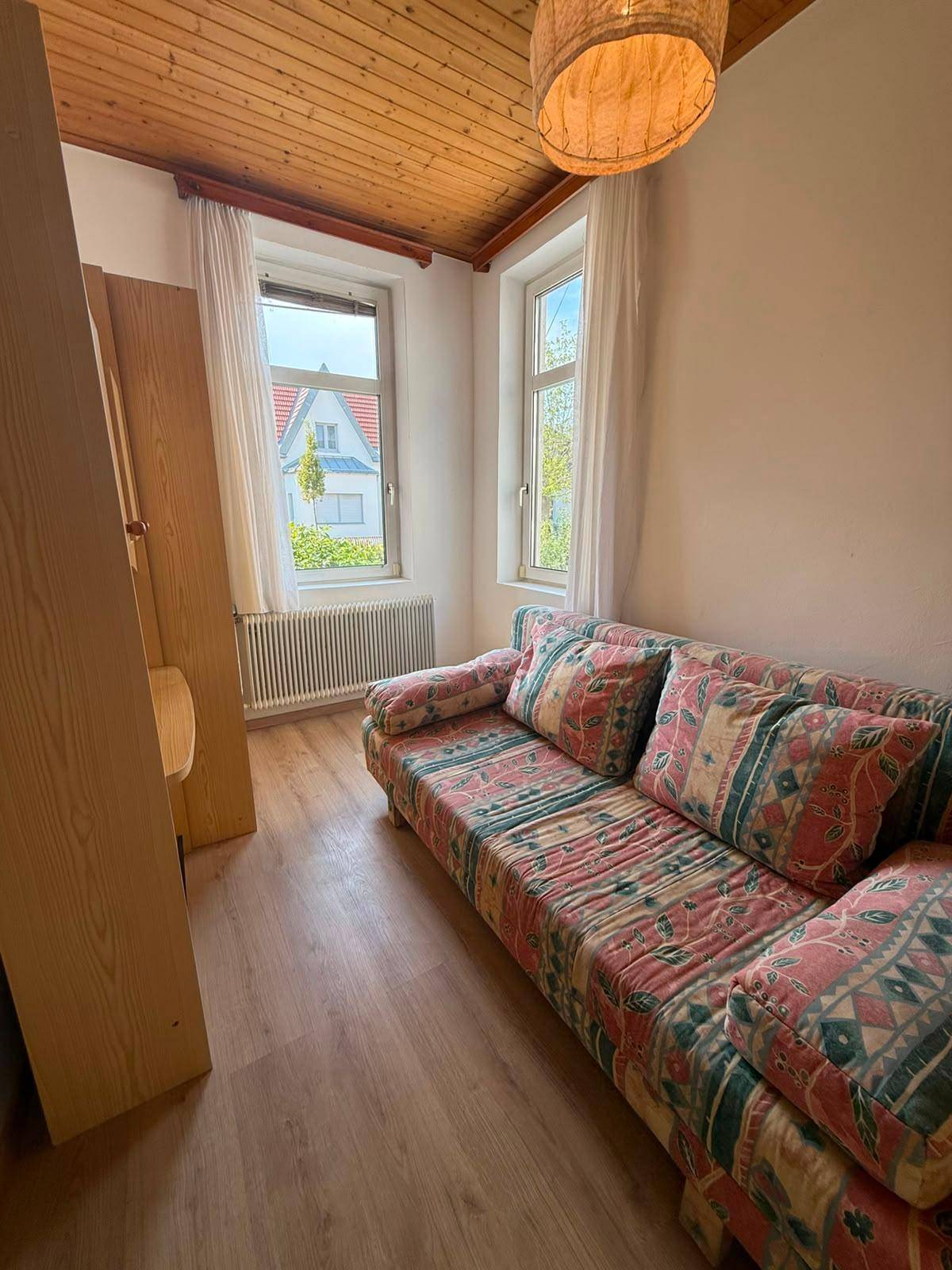 Schlafzimmer mit gemustertem Schlafsofa, Holzdecke und Laminatboden, hell und freundlich.