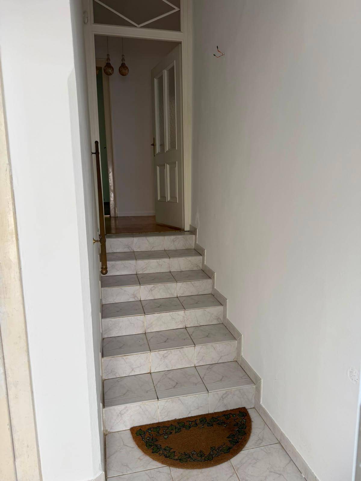 Innenliegende Treppe mit hellen Fliesenstufen und einem Teppichläufer am Eingang.