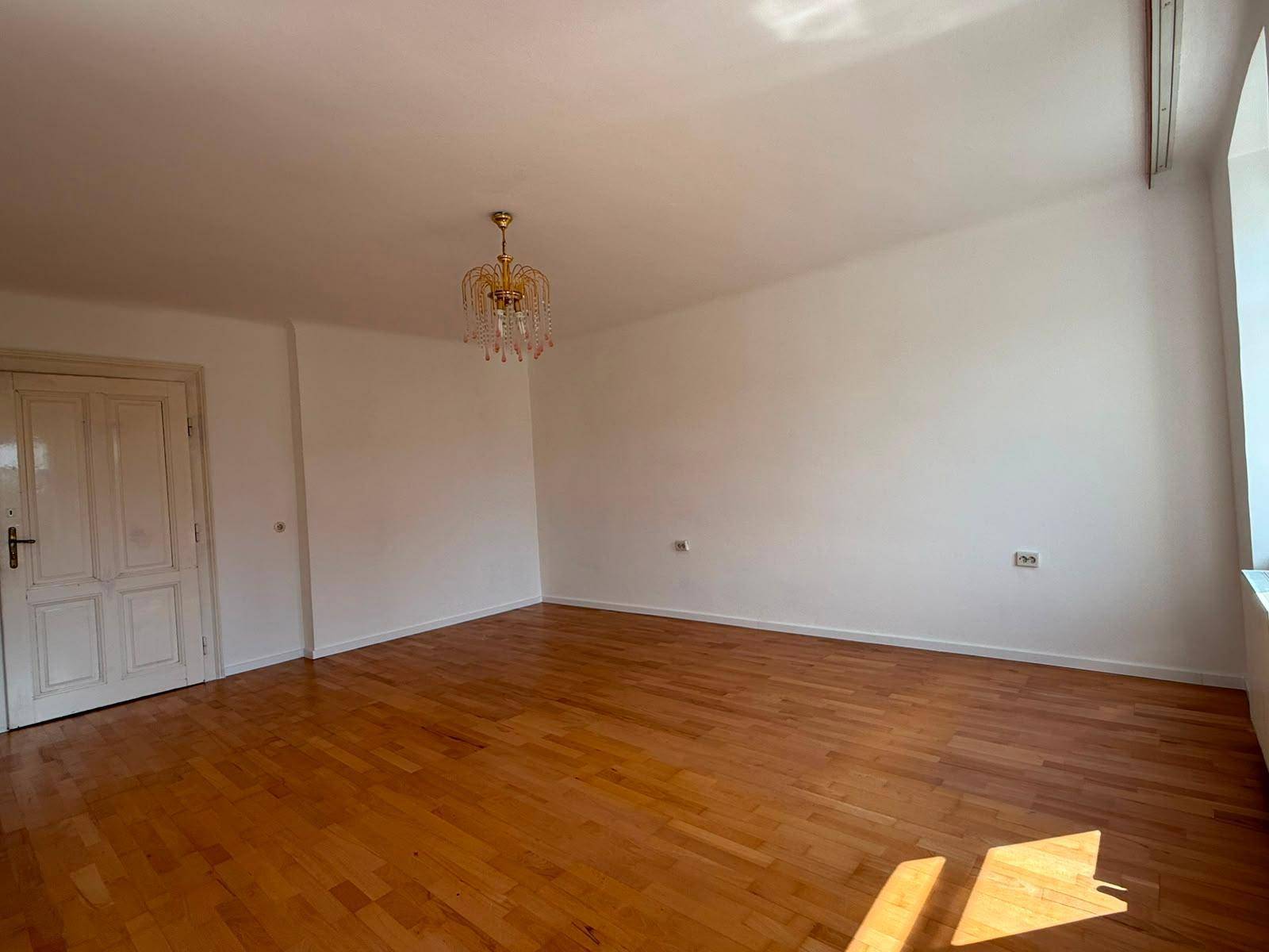 Helles Wohnzimmer mit Parkettboden, weiß gestrichenen Wänden und einem eleganten Kronleuchter.