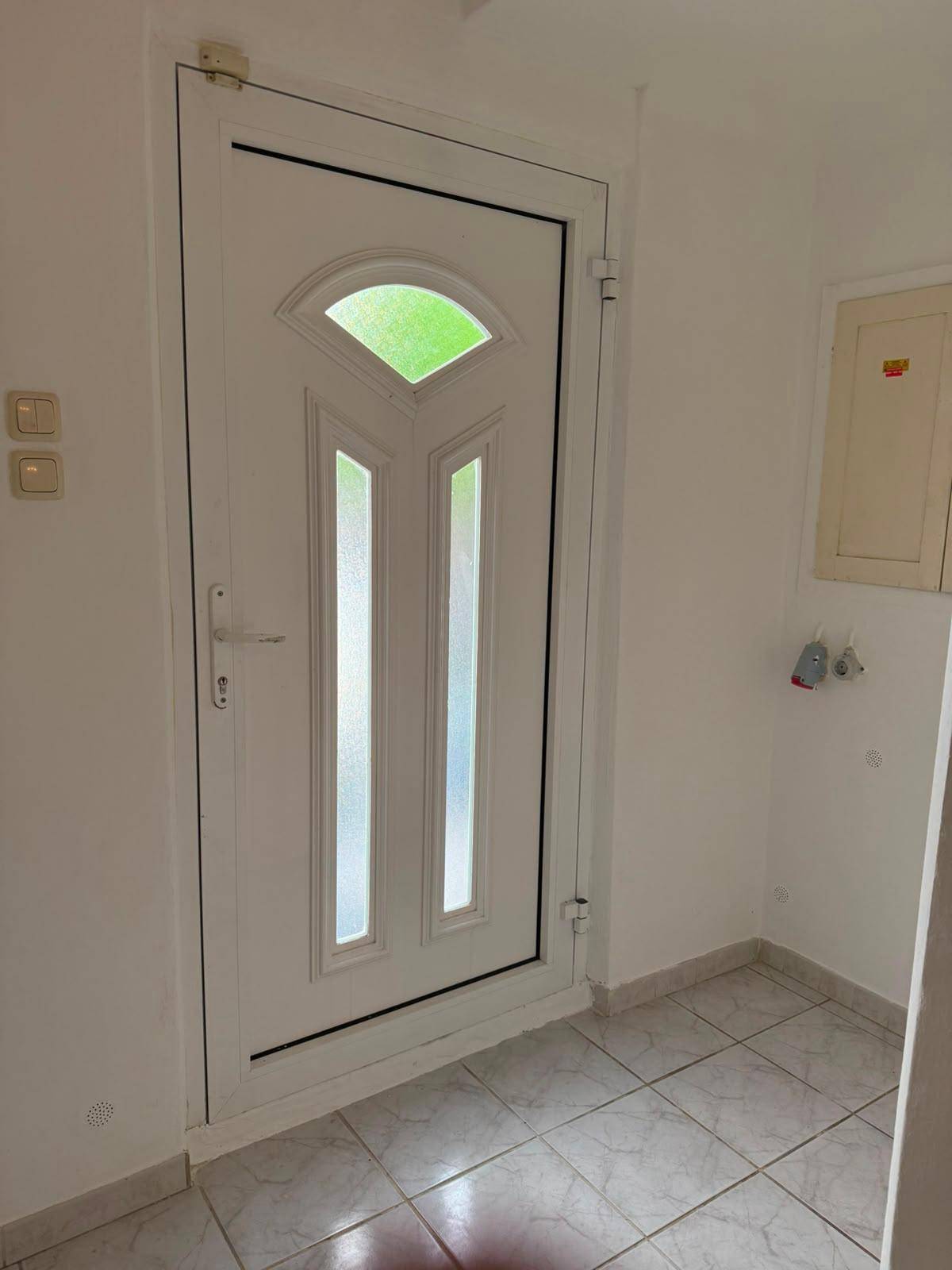 Weiße Eingangstür mit Glaseinsätzen und Fliesenboden im Eingangsbereich.