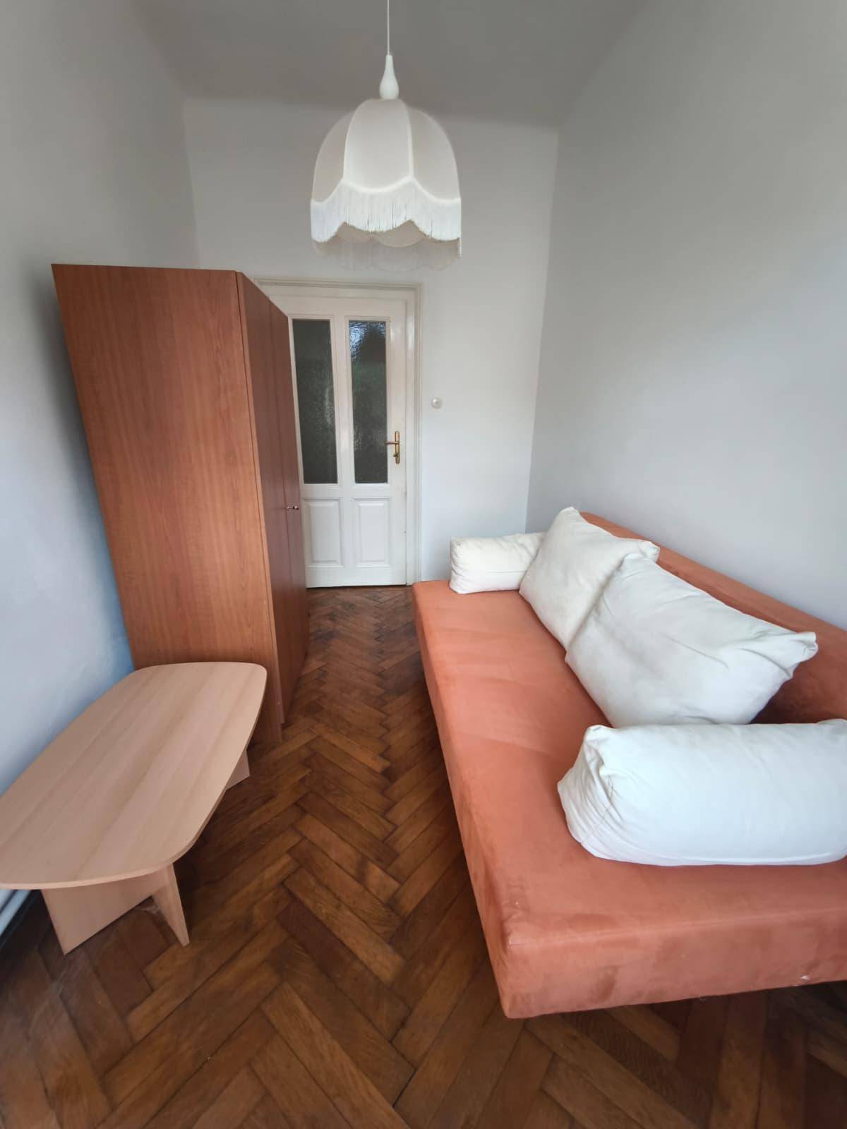 Ansicht des kleinen Zimmers mit Holzschrank, Sofa und einer weißen Tür, hell und funktional.