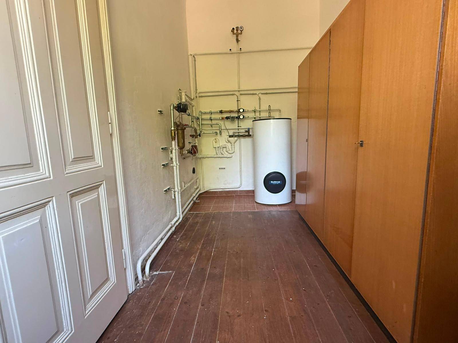 Hauswirtschaftsraum mit Warmwasserspeicher, sichtbaren Rohren und Holzschränken für Stauraum.