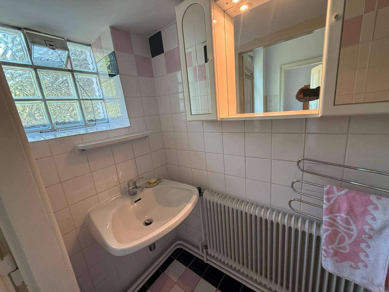 Badezimmer mit Waschbecken, Spiegelschrank, Heizkörper und rosa-weißen Fliesen.
