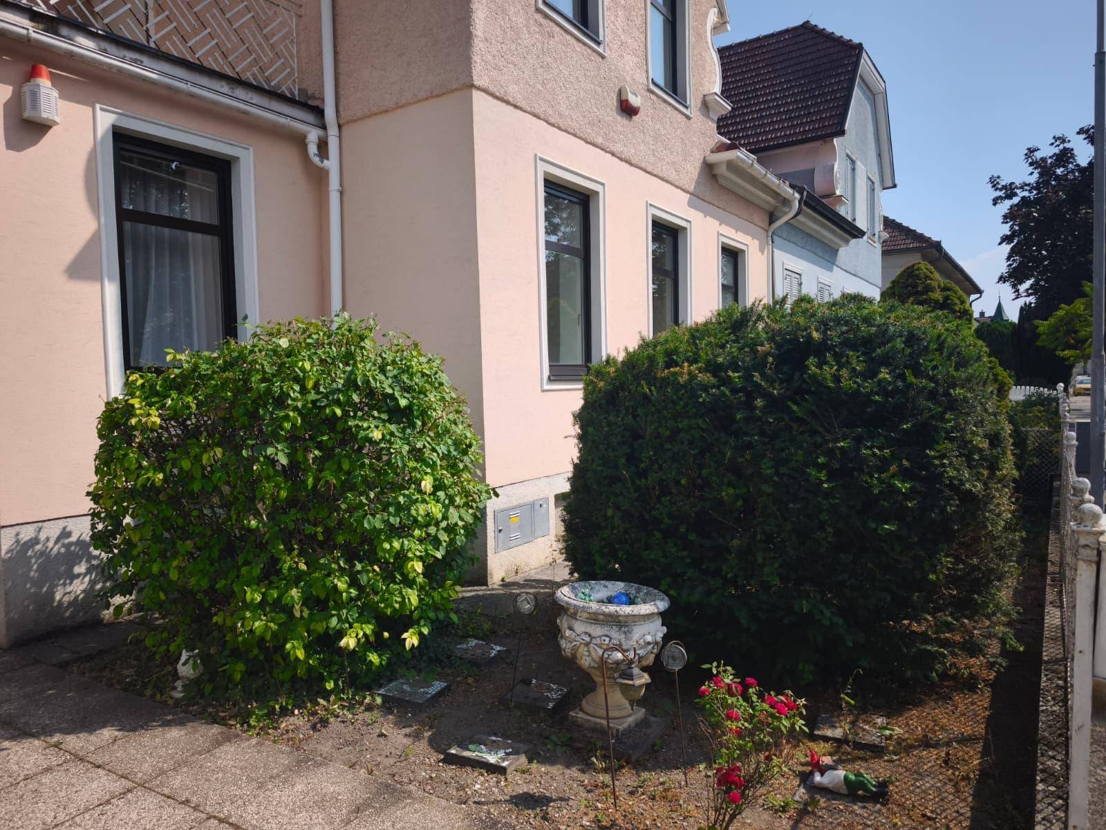 Kleiner Vorgartenbereich mit dichten Büschen, einer dekorativen Urne und der Hausfassade.