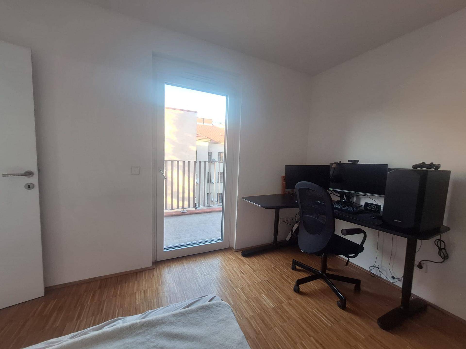 Schlafzimmer mit Arbeitsplatz und direktem Zugang zu einem sonnigen Balkon, bietet viel Tageslicht.