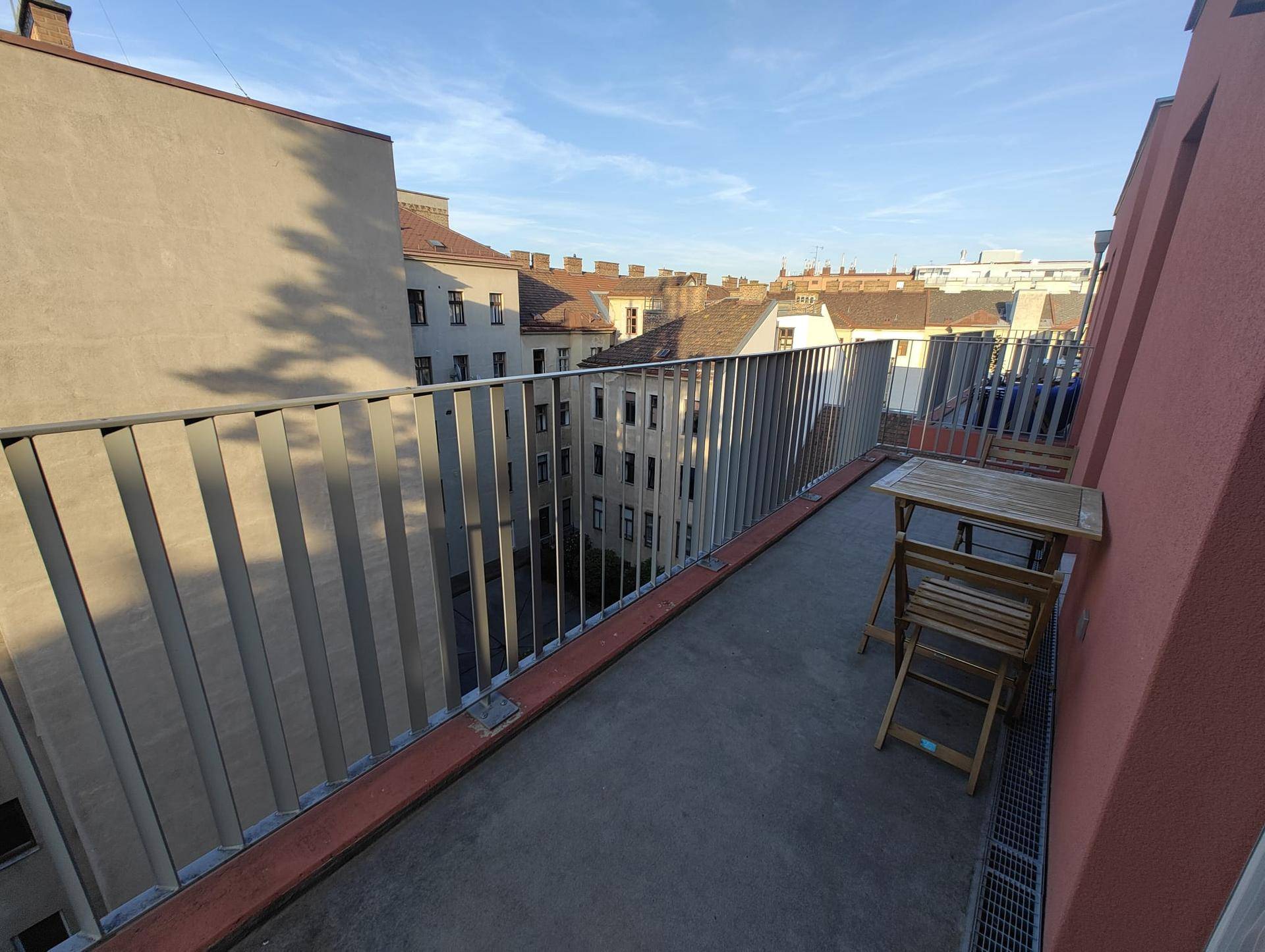 Sonniger Balkon mit Holztisch und Stühlen, bietet einen Blick auf die umliegenden Gebäude.