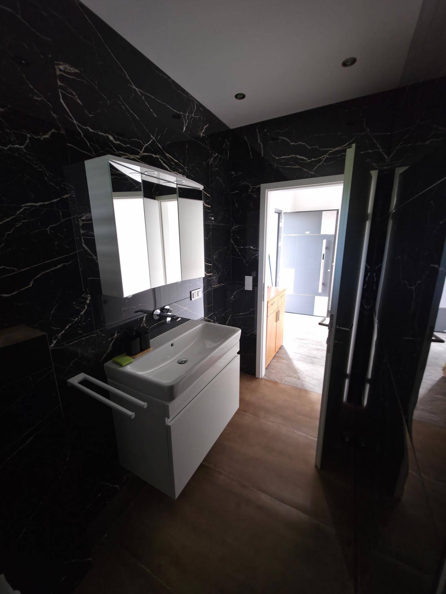 Stilvolles Badezimmer mit Waschtisch, Spiegelschrank und dunklen Marmorfliesen.