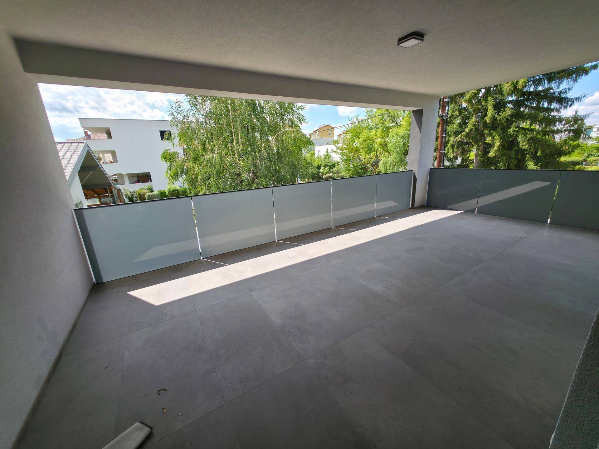 Geräumiger überdachter Balkon mit Fliesenboden und Blick ins Grüne.