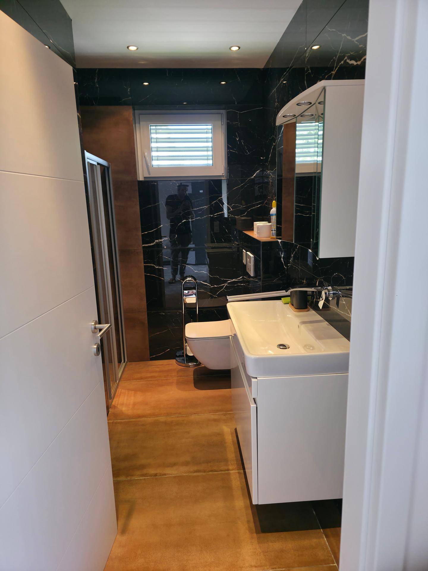 Elegantes Badezimmer mit Waschtisch, Toilette, Fenster und schwarzen Marmorfliesen.