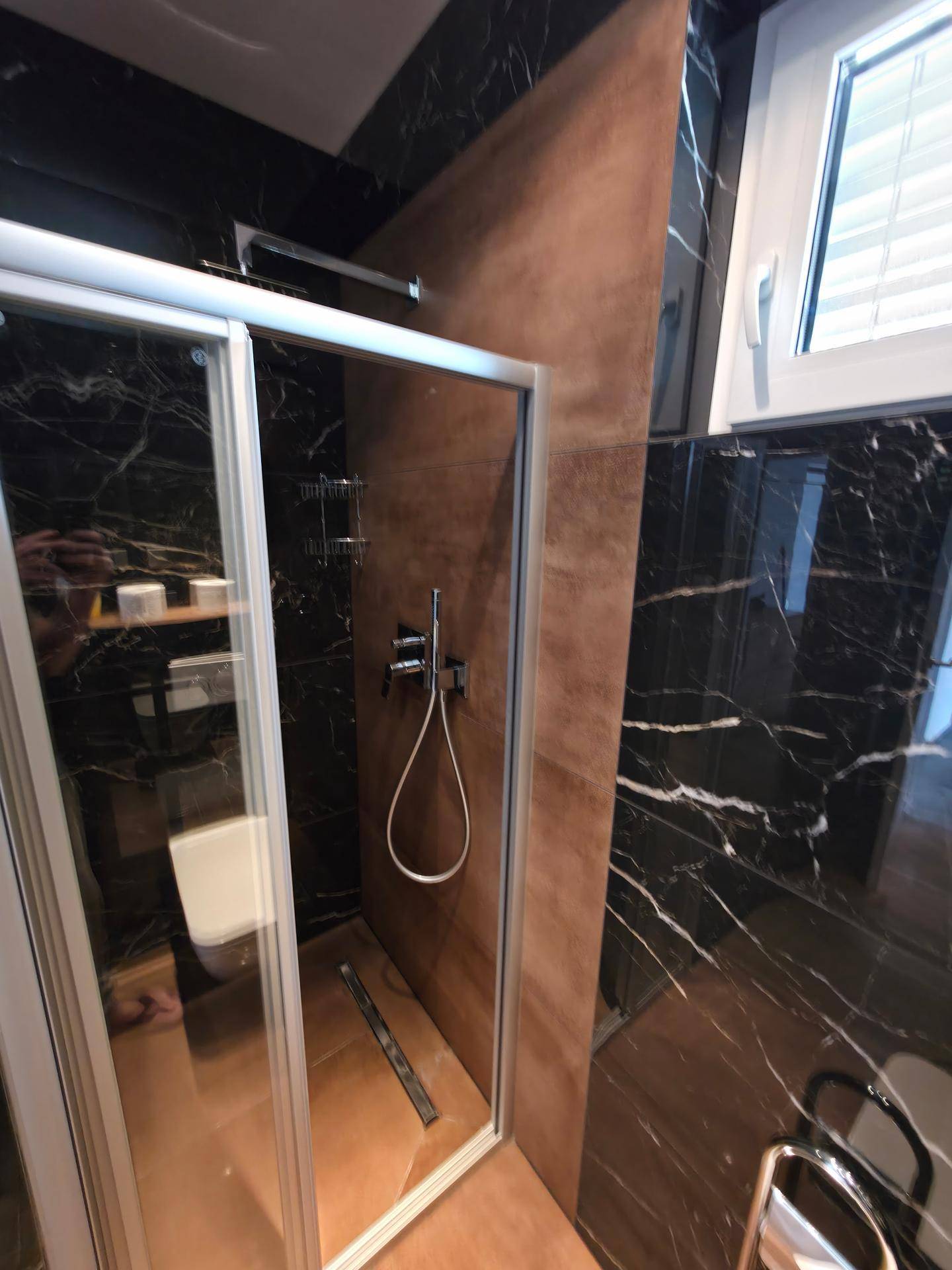 Moderne Dusche mit schwarzen Marmorfliesen und brauner Akzentwand im Badezimmer.