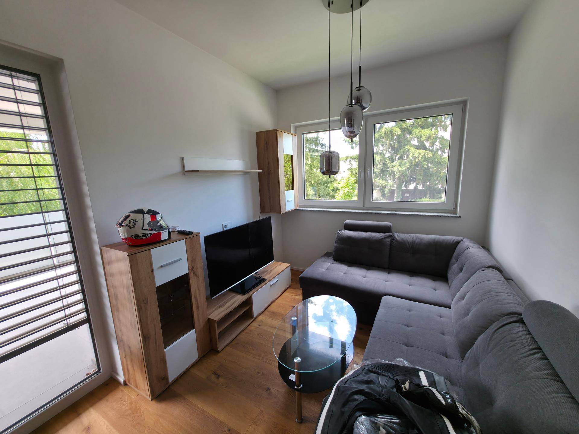 Gemütliches Wohnzimmer mit grauem Ecksofa, TV-Möbeln und Zugang zum Balkon.