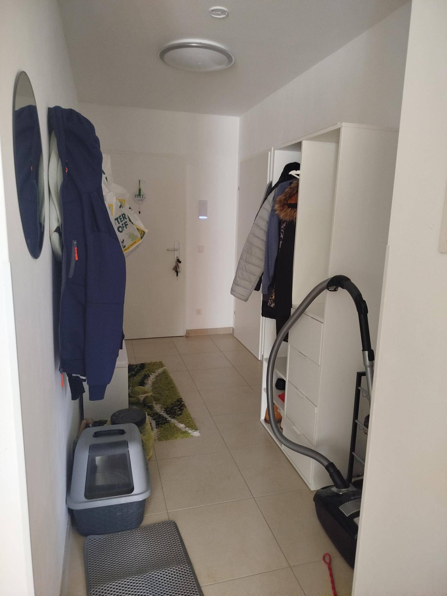 Heller Flur mit Fliesenboden, Garderobe und praktischem Stauraum für Haushaltsgeräte.