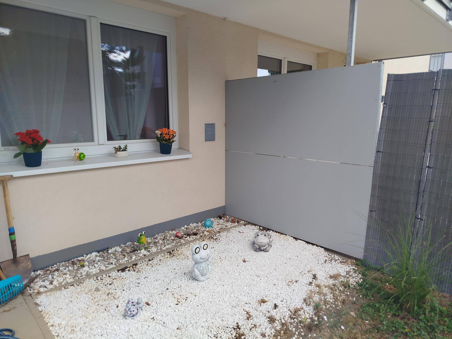 Kleiner Ziergarten mit weißen Kieselsteinen und Gartenzwergen neben der Hauswand.