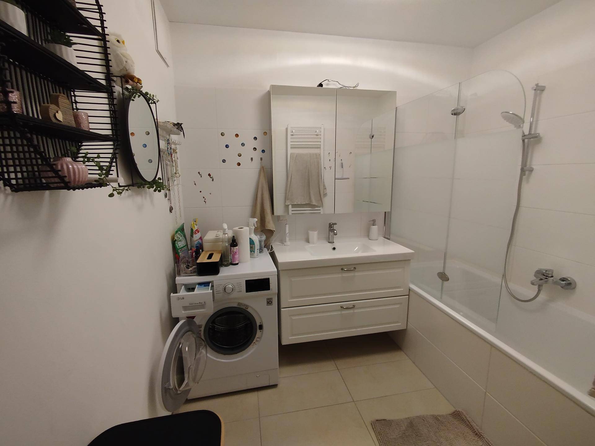 Helles Badezimmer mit Badewanne, Waschbeckenunterschrank, Spiegelschrank und Waschmaschine.