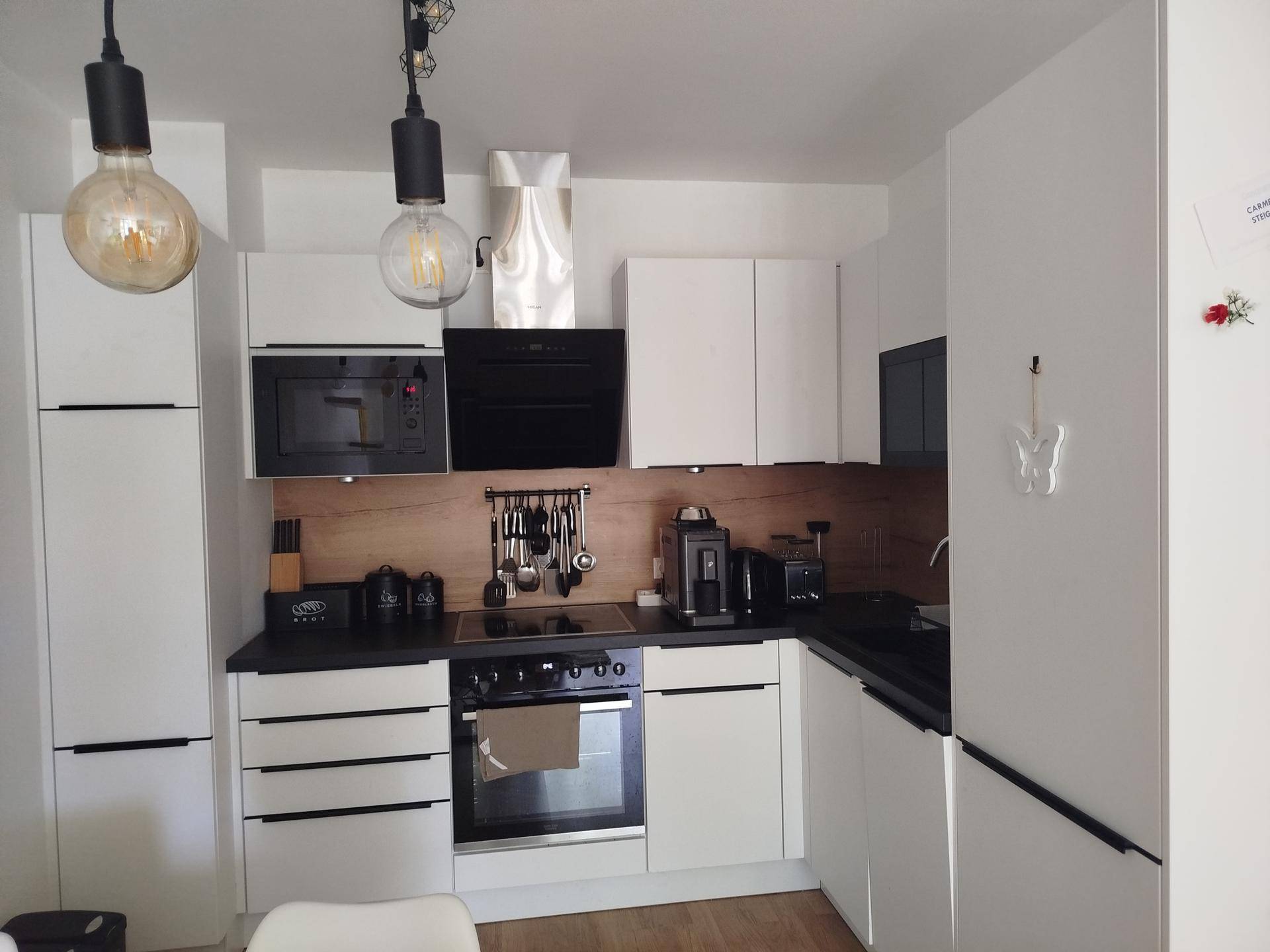 Moderne Küche mit weißen Schränken, schwarzen Arbeitsplatten und integrierten Geräten für effizientes Kochen.