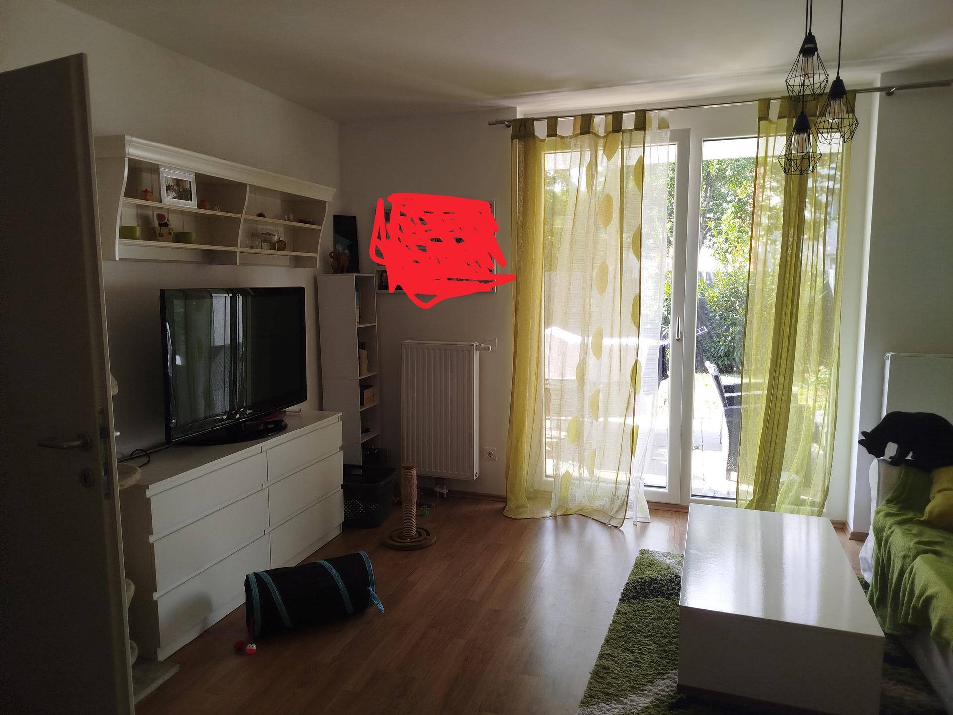 Wohnzimmer mit Fernseher, Kommode und großem Glaszugang zu einem sonnigen Außenbereich.