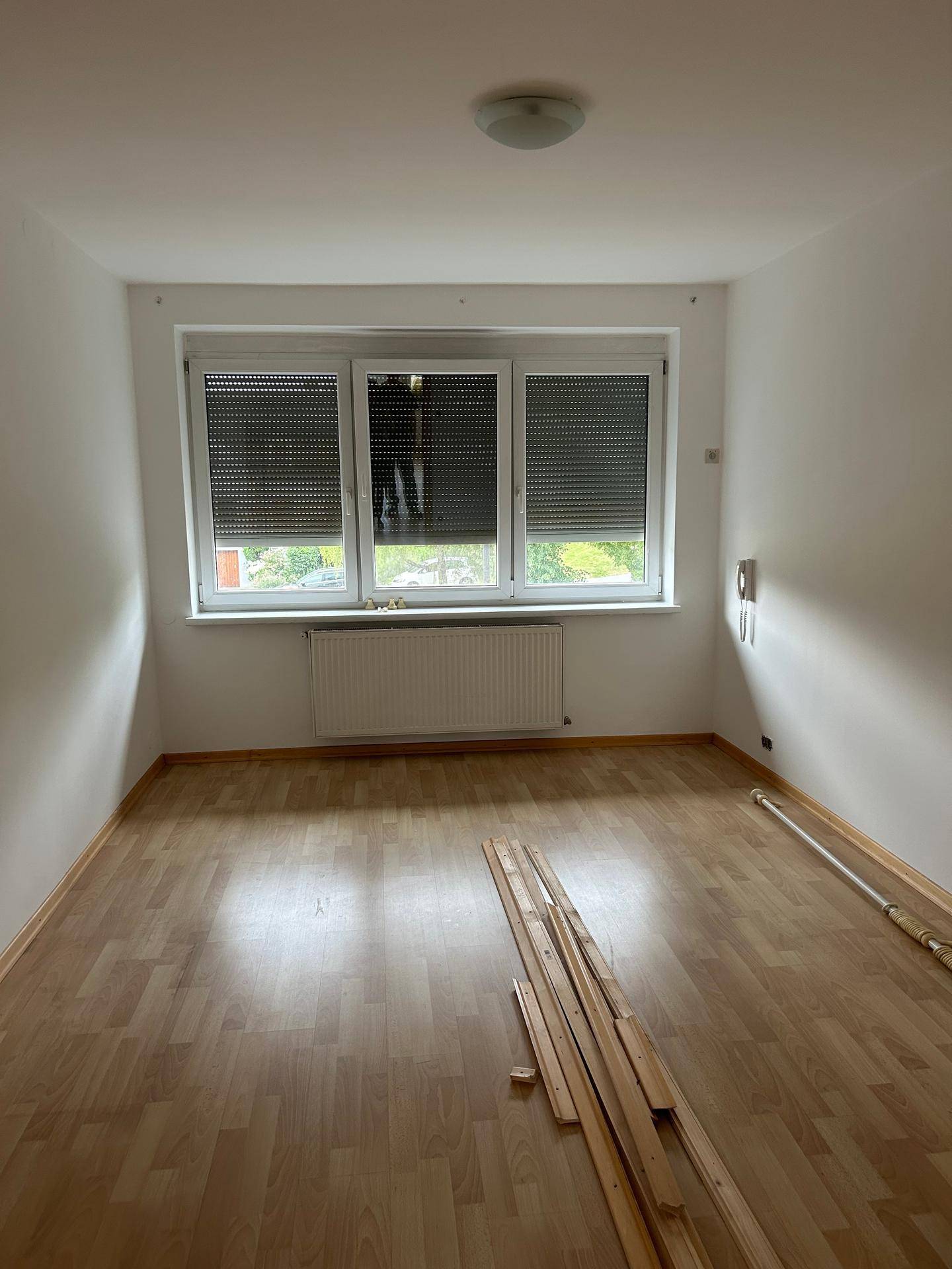 Helles Schlafzimmer mit Laminatboden und Fenster mit Rollläden, ideal für Ruhe und Erholung.